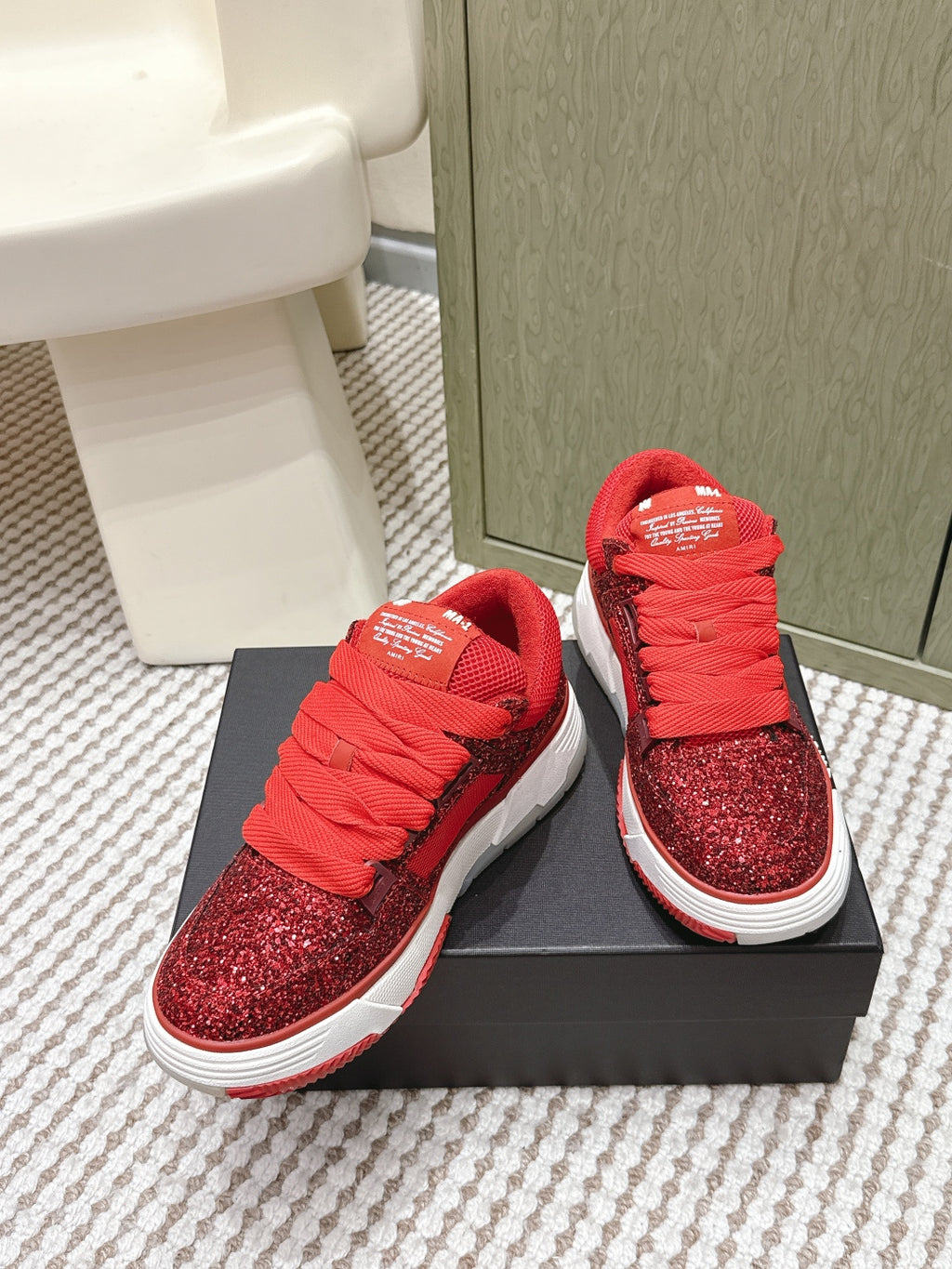 Red glitter lace-up sneakers with striped white sole, on black box