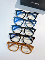 Assorted Prada eyeglasses in black, blue, and amber full-rim frames laid out.