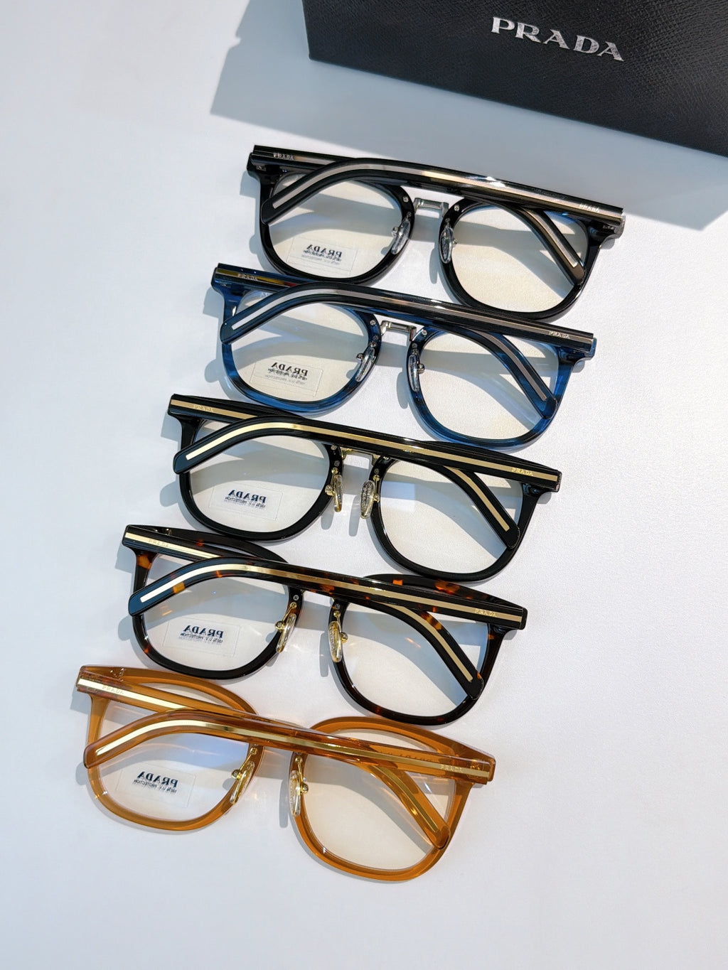 Assorted Prada eyeglasses with black, blue, and brown full-rim frames laid out.