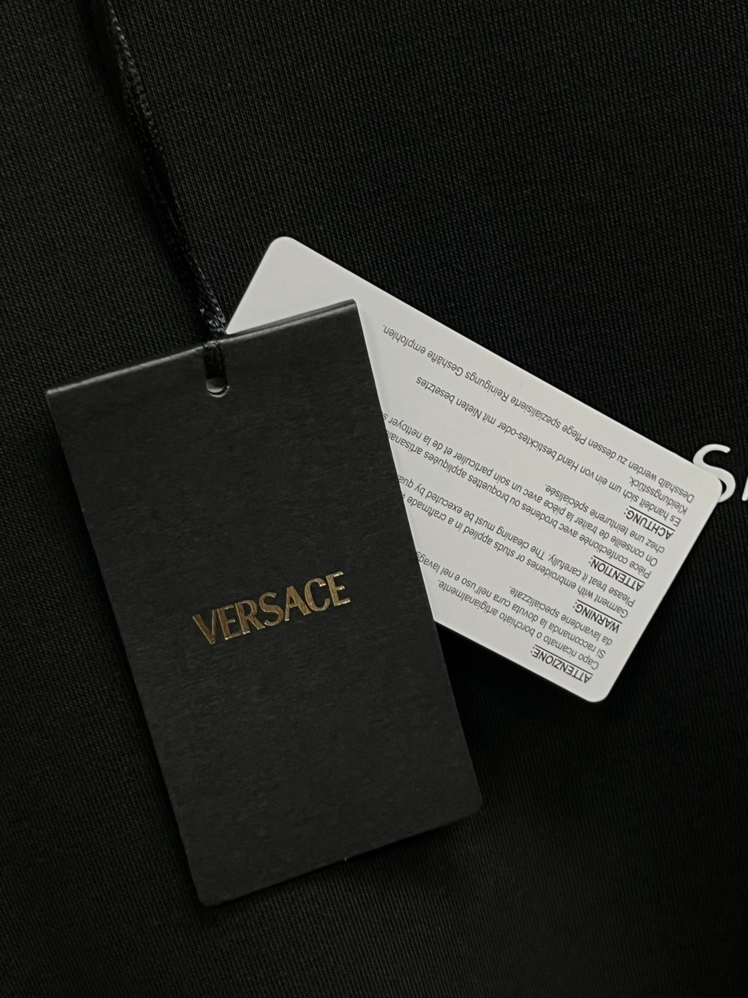 Versace hang tags attached to a dark gray crewneck sweatshirt