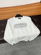 White crewneck sweatshirt with rhinestone logo on chest, folded on seat