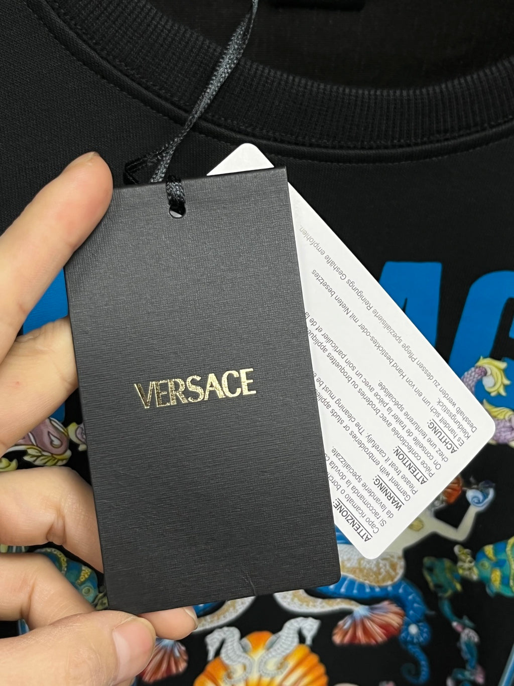 Black crewneck sweatshirt with Versace hang tag and care label