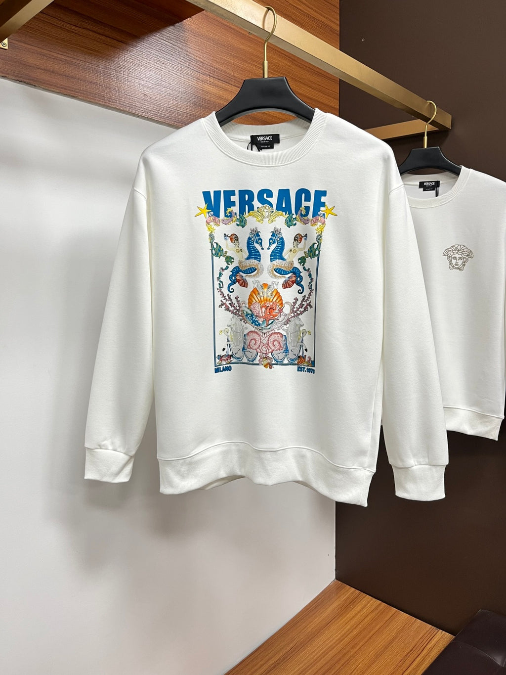 White sweatshirt with colorful crest graphic and blue VERSACE logo on chest