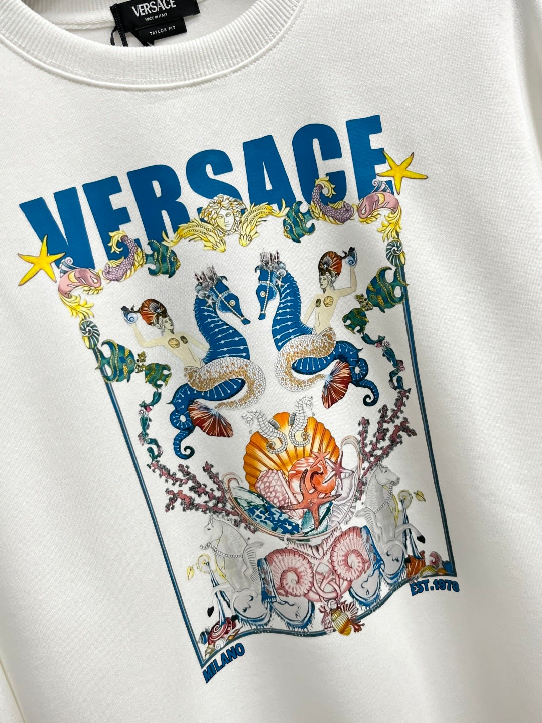 White sweatshirt with large colorful crest illustration and VERSACE lettering