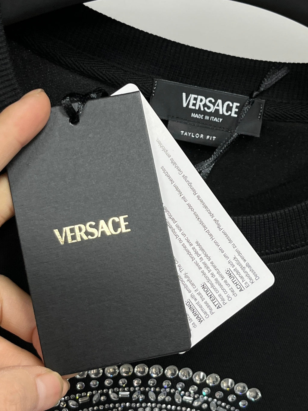 Black sweatshirt with hanging VERSACE brand label and care tag near collar