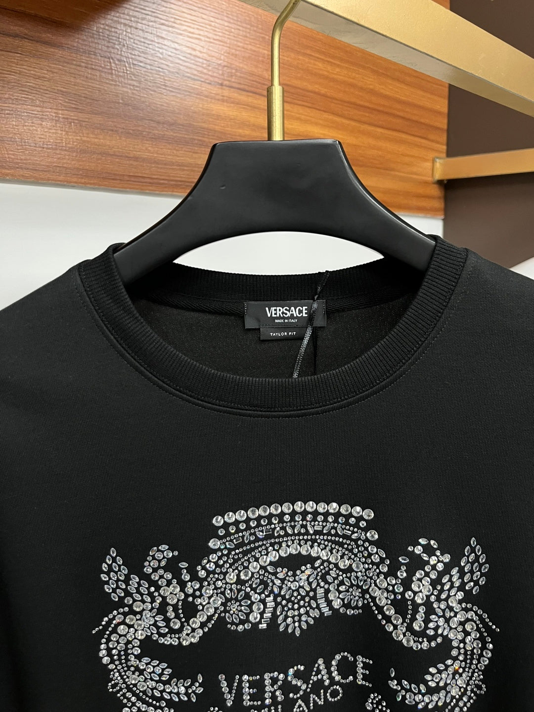 Black crewneck sweatshirt neckline with partial rhinestone Medusa crest logo