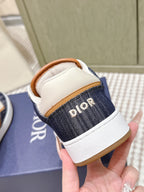 Back view of navy low-top sneakers with white heel, tan collar, and Dior “R” text