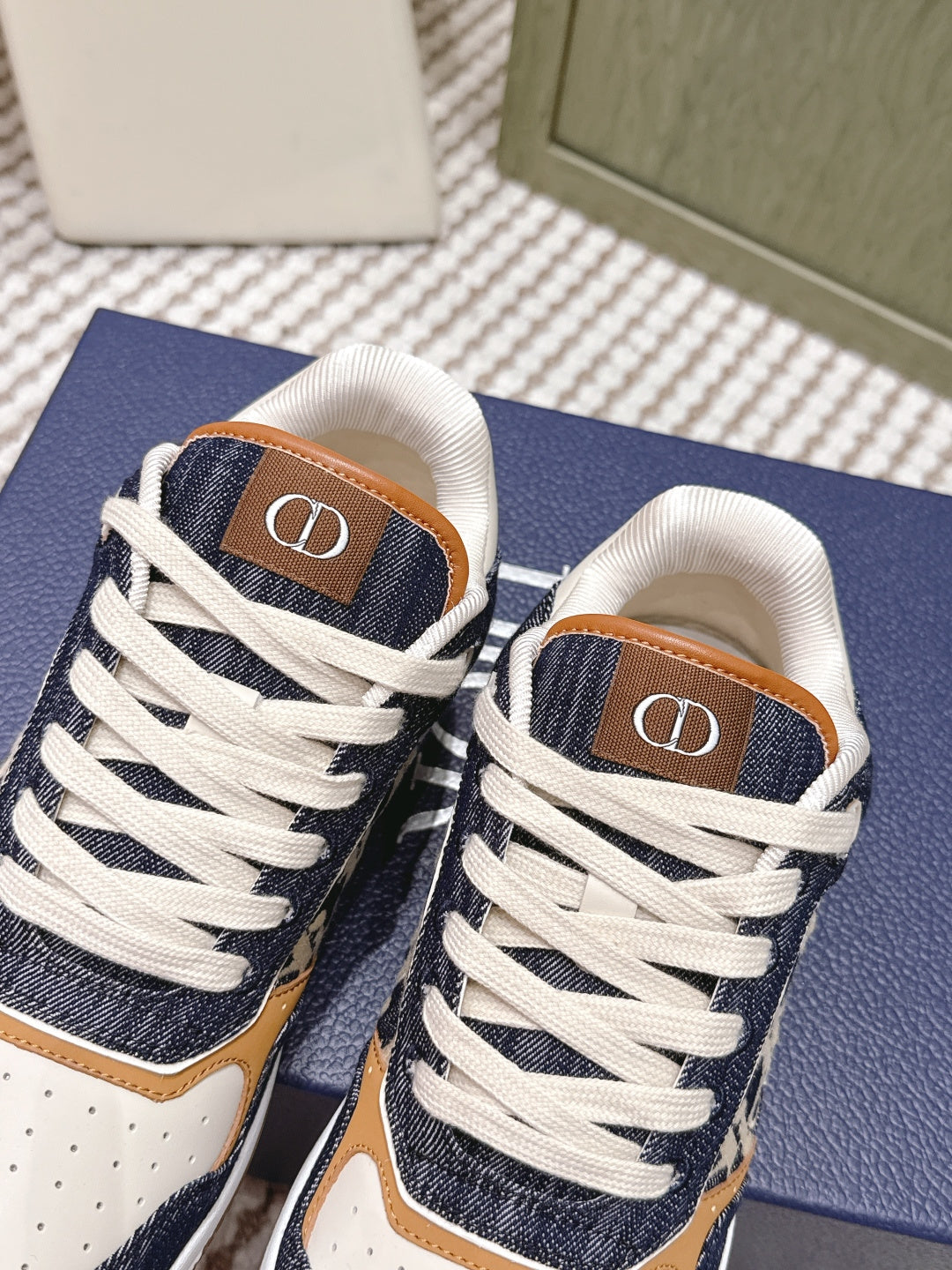 Navy-and-cream low-top sneakers with white laces and tan “D” logo on tongue