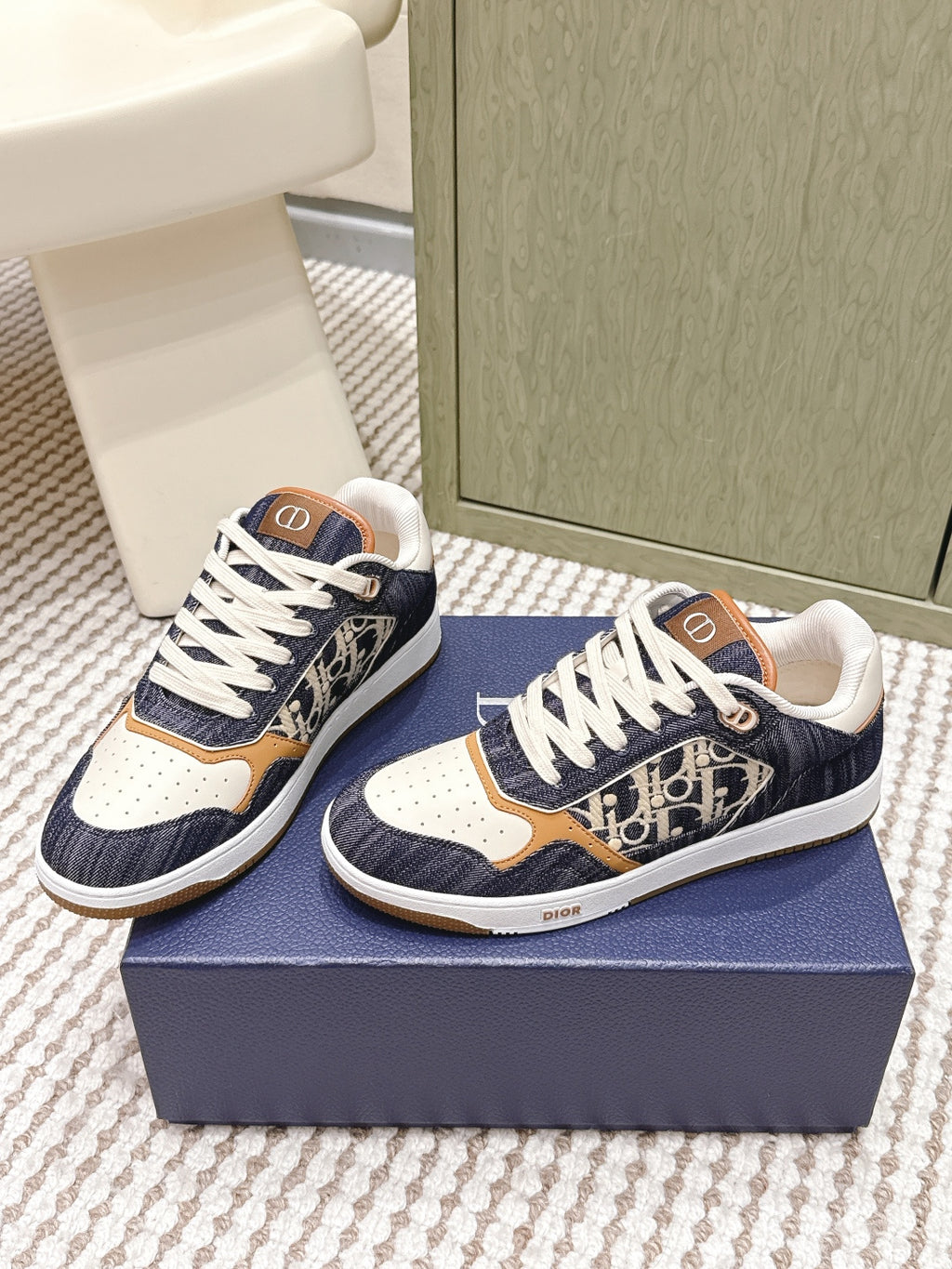 Navy low-top sneakers with white laces, tan and cream panels, and Dior “D” emblem accents