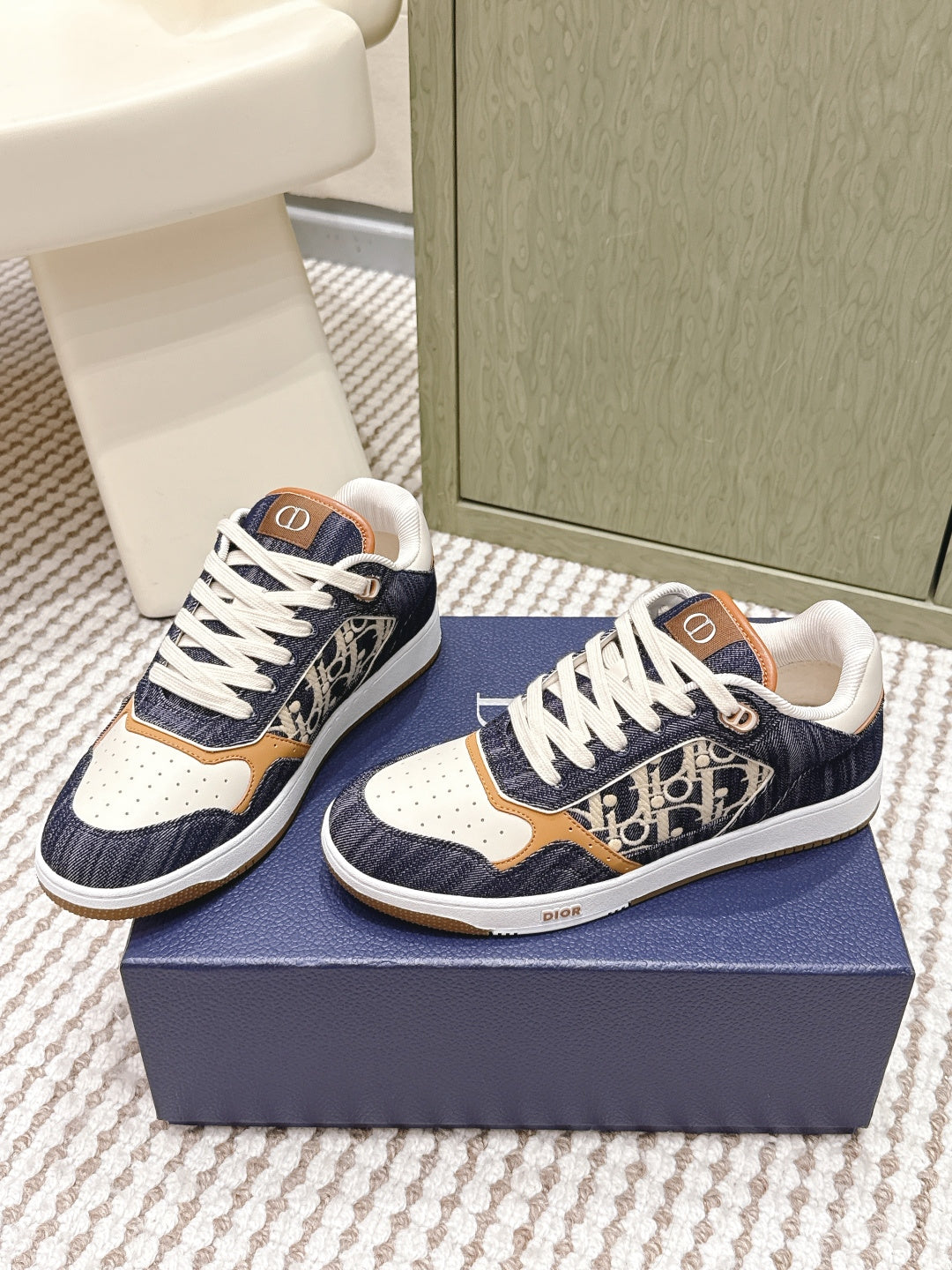Navy low-top sneakers with white laces, tan and cream panels, and Dior “D” emblem accents