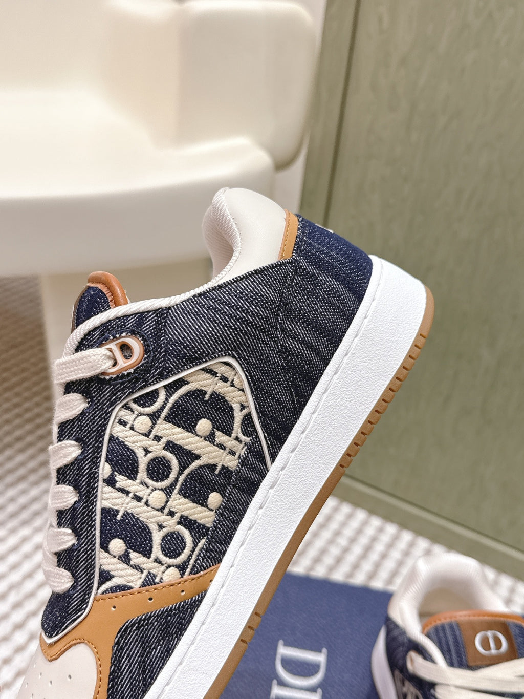 Close-up of navy low-top sneaker side with Dior monogram, tan accents, and white laces