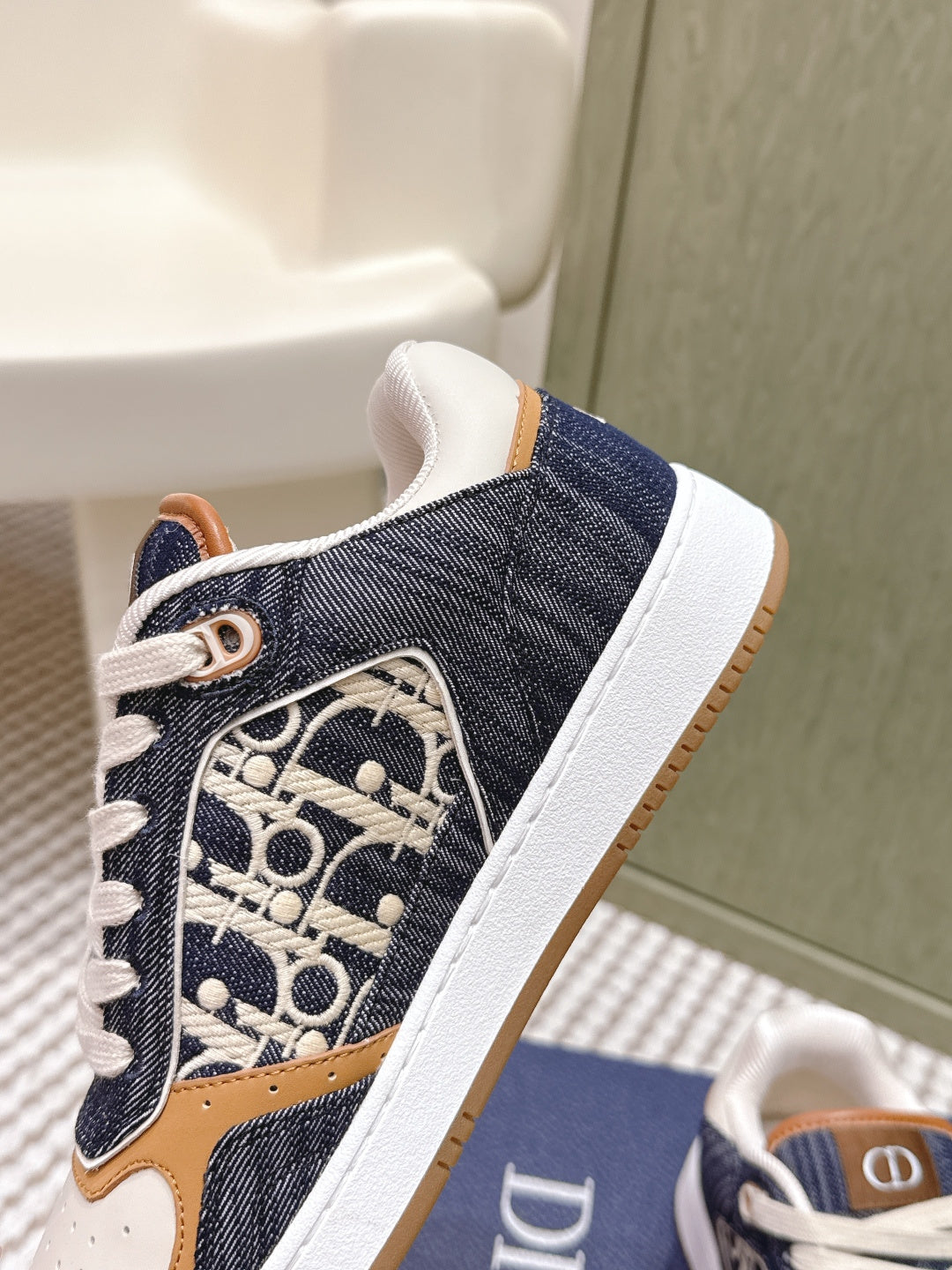 Close-up of navy low-top sneaker side with Dior monogram, tan accents, and white laces