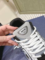 Close-up of Dior sneakers: gray panel, white laces, and logo patch.