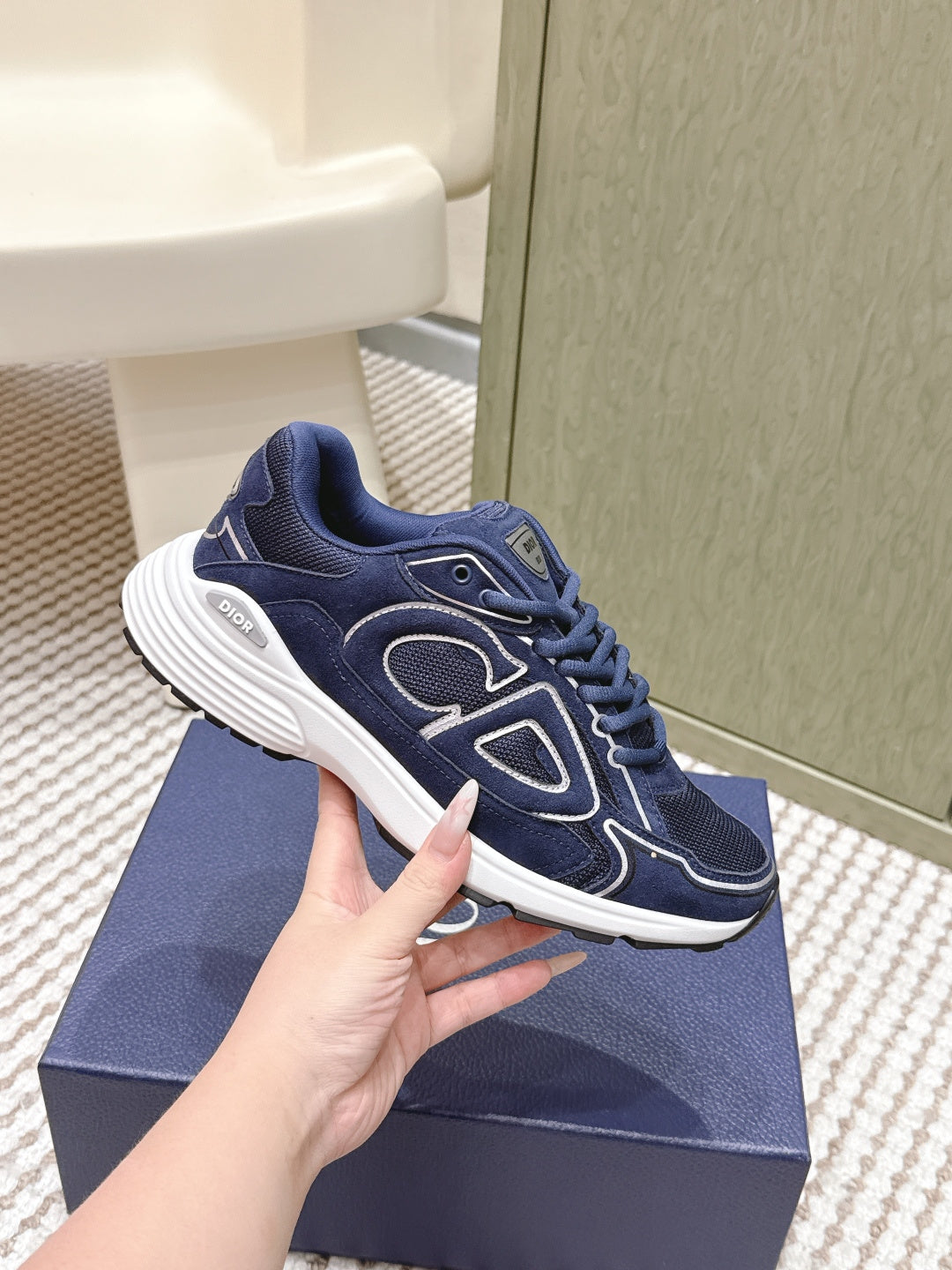 Navy Dior unisex sneakers in hand; side profile with white sole and logo detailing