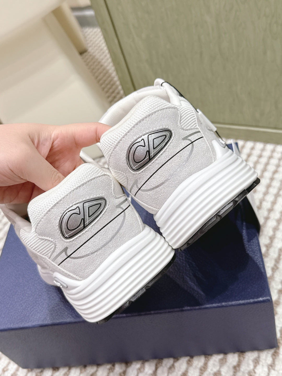 White Dior sneakers close-up of heel side emblems and ribbed sole, held by hand.