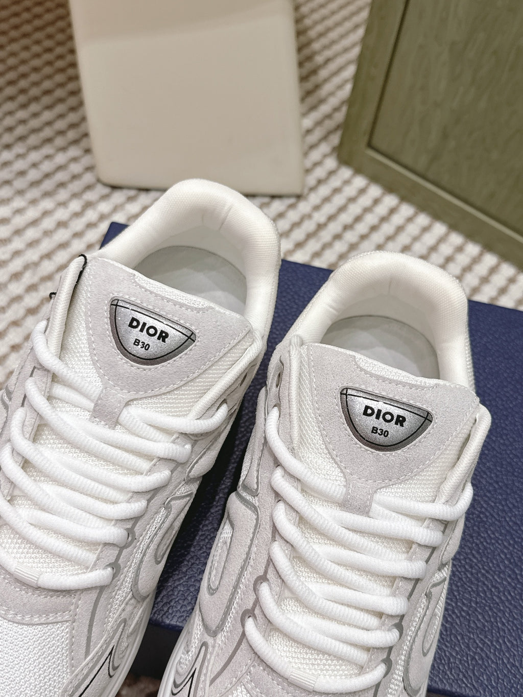 White Dior sneakers close-up of tongues and lace-up vamps, on navy box.