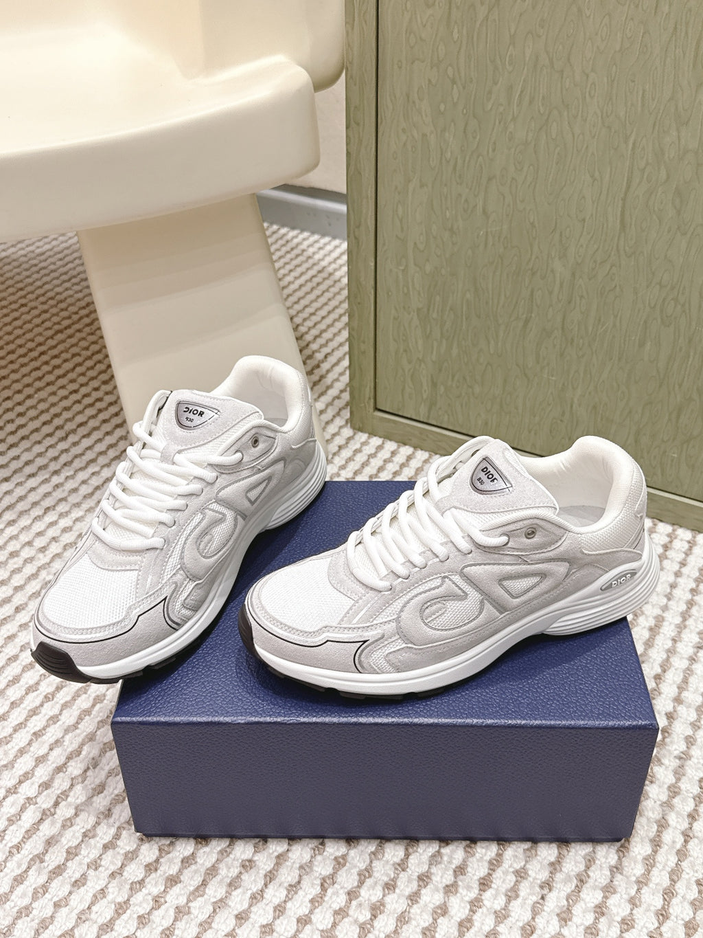 White Dior low-top sneakers, side view, with raised textured logo and laces.
