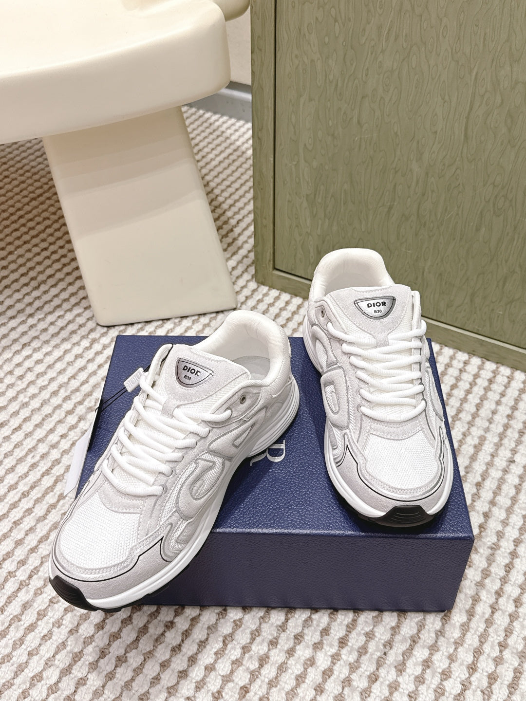 White Dior low-top sneakers, front three-quarter view, on navy shoebox.
