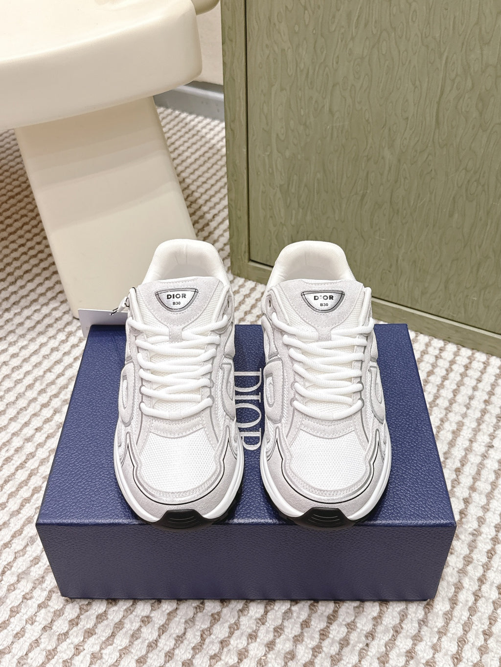 White Dior low-top sneakers with lace-up front and thick rubber sole on box.