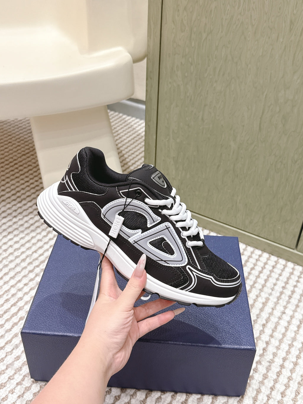 Black and white Dior unisex sneaker held in hand, side and outsole view