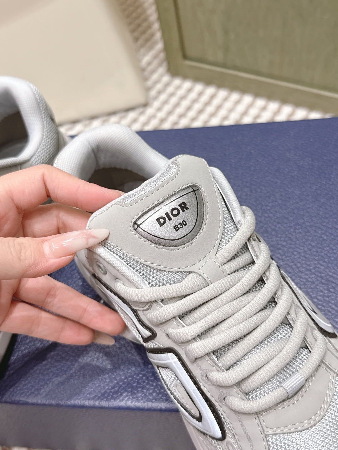 Unisex sneaker tongue label with Dior-style logo; light gray/white lace-up upper