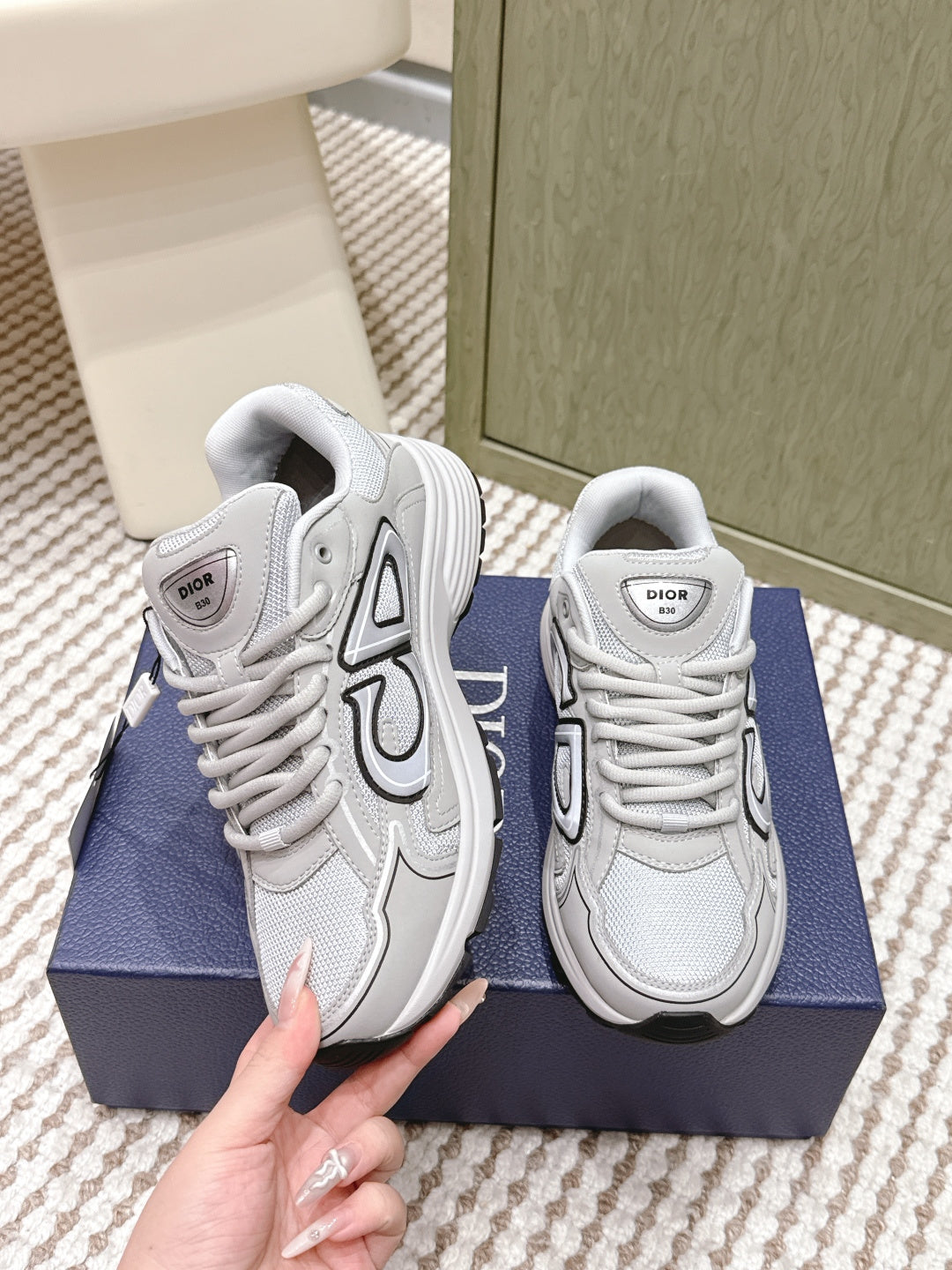 Unisex lace-up sneakers in light gray/white with Dior logo patch, held by hand