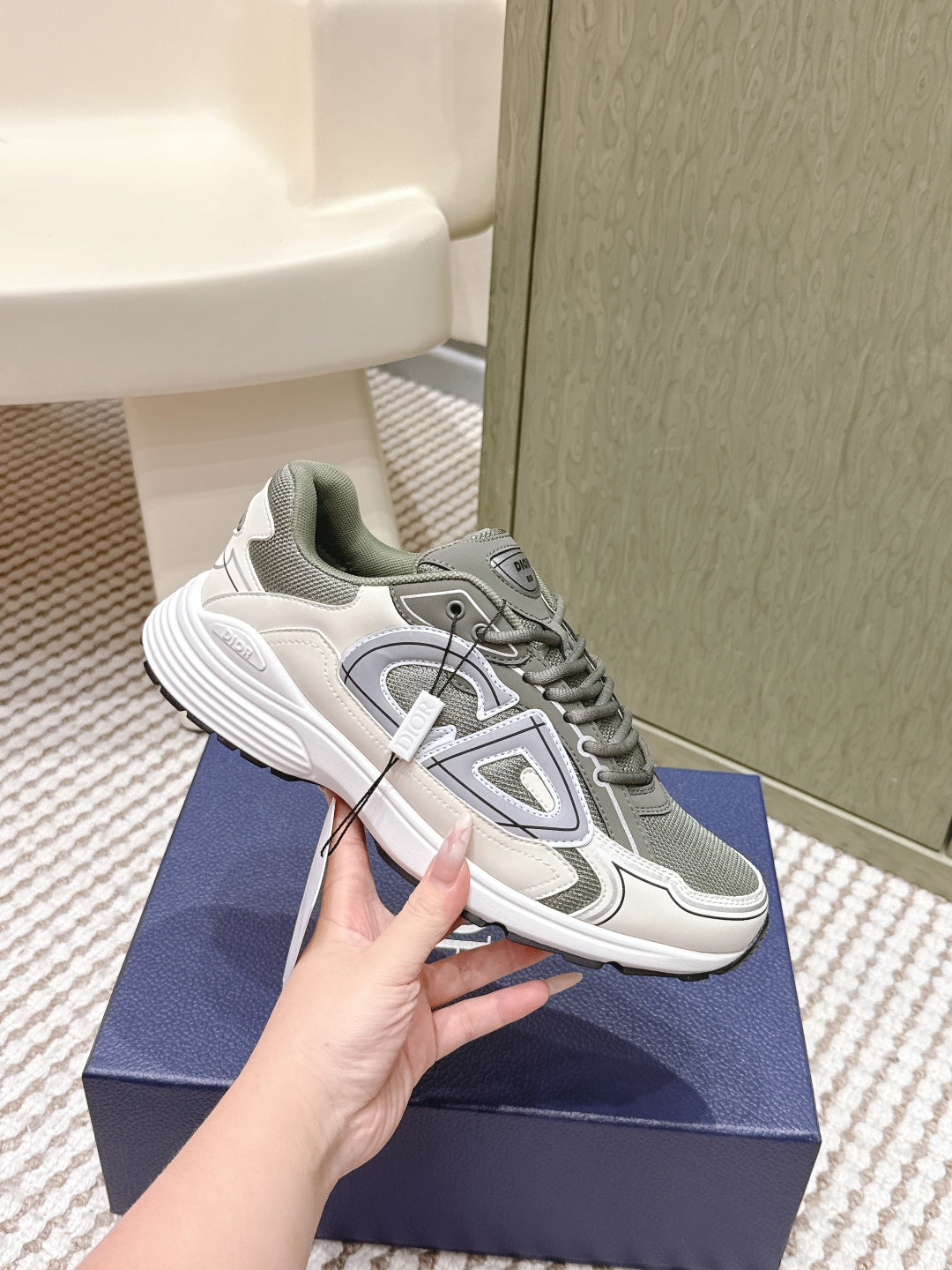 Grey and white lace-up sneakers with side emblem detailing, held above the box
