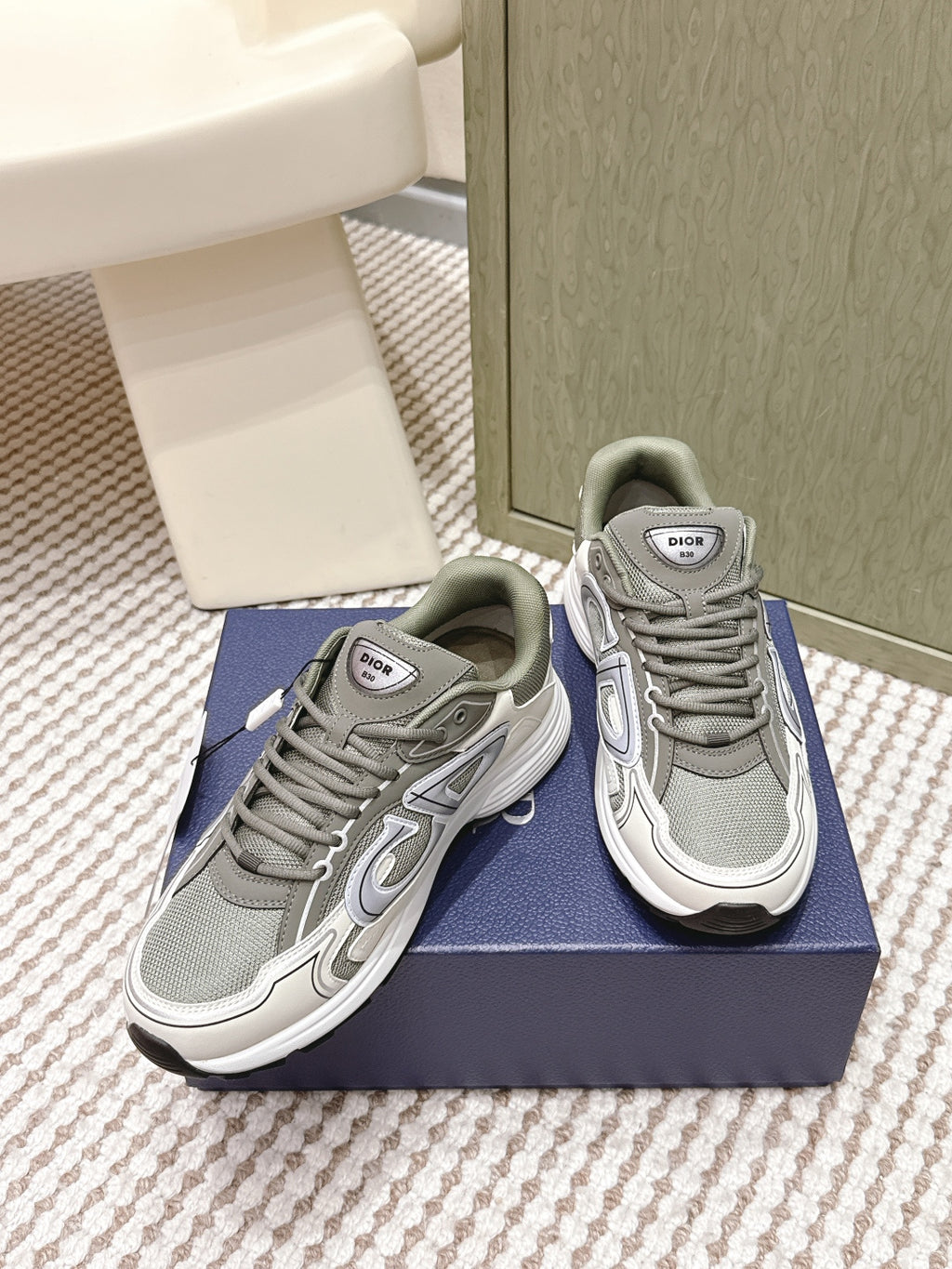 Grey lace-up sneakers with white trim and Dior logo tongue labels on the box