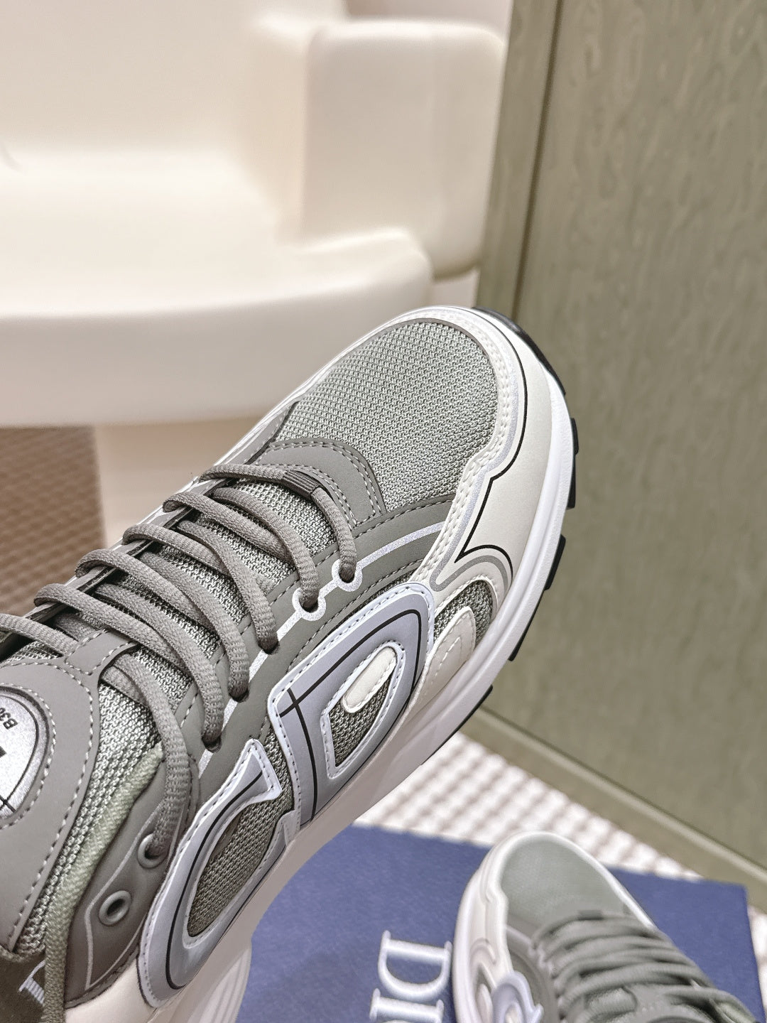 Grey sneaker side view with white midsole, tread sole, and Dior branding on upper