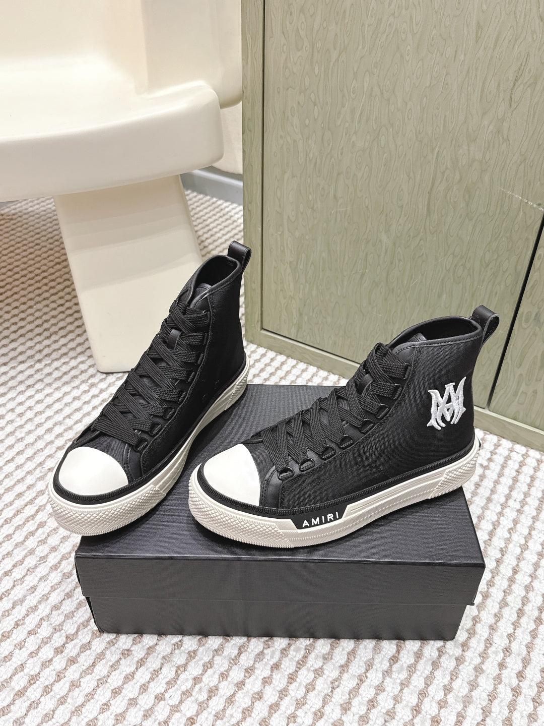 Amiri black mid-top sneakers on a box, white rubber sole and lace-up front