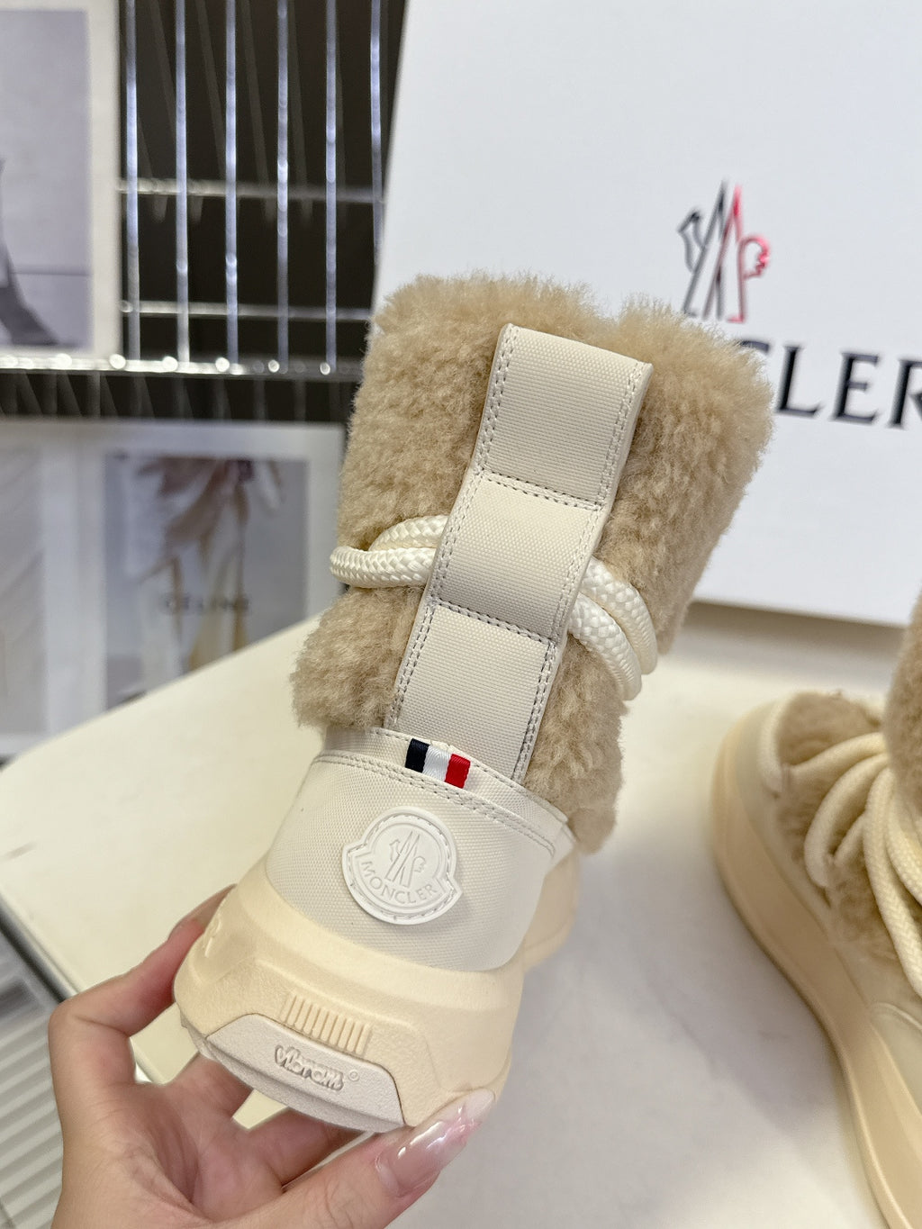 Beige shearling lace-up boot held in hand, with strap detail and logo badge