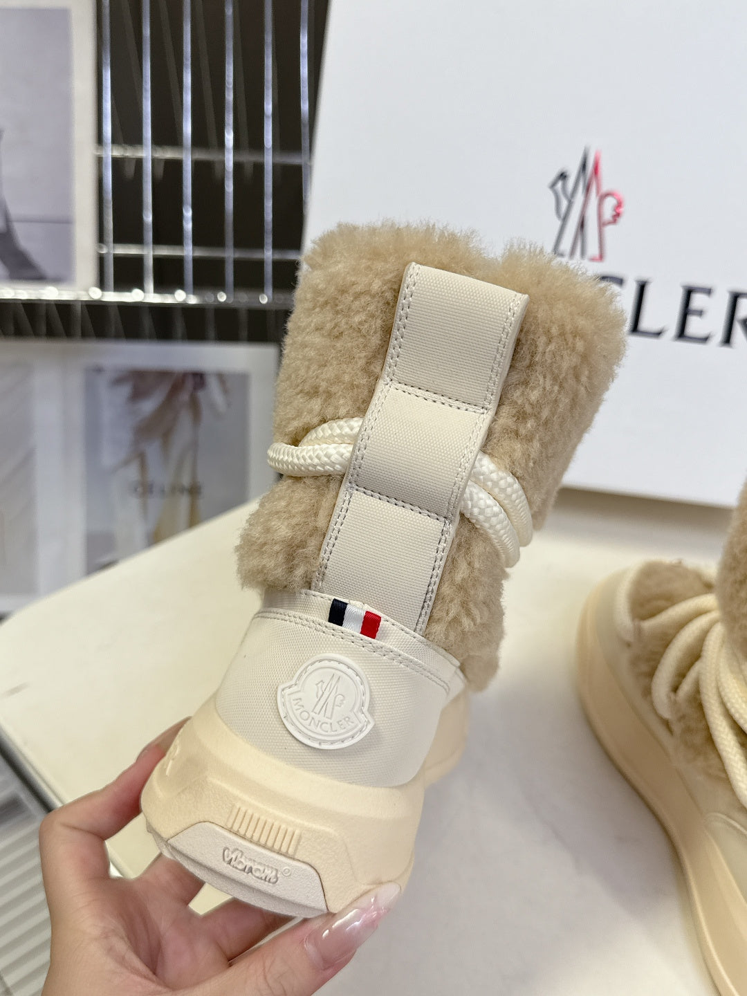 Beige shearling lace-up boot held in hand, with strap detail and logo badge