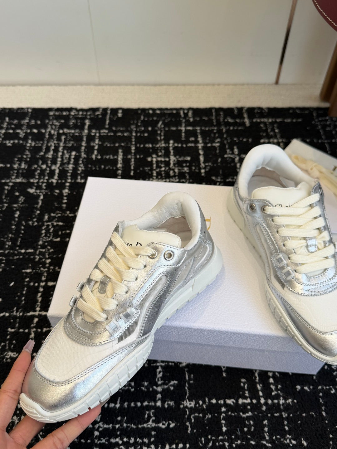 White Dior low-top sneakers, held by hand on box, lace-up design