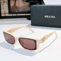 Prada sunglasses with cream frame, oversized brown lenses, gold triangle logo at temples.