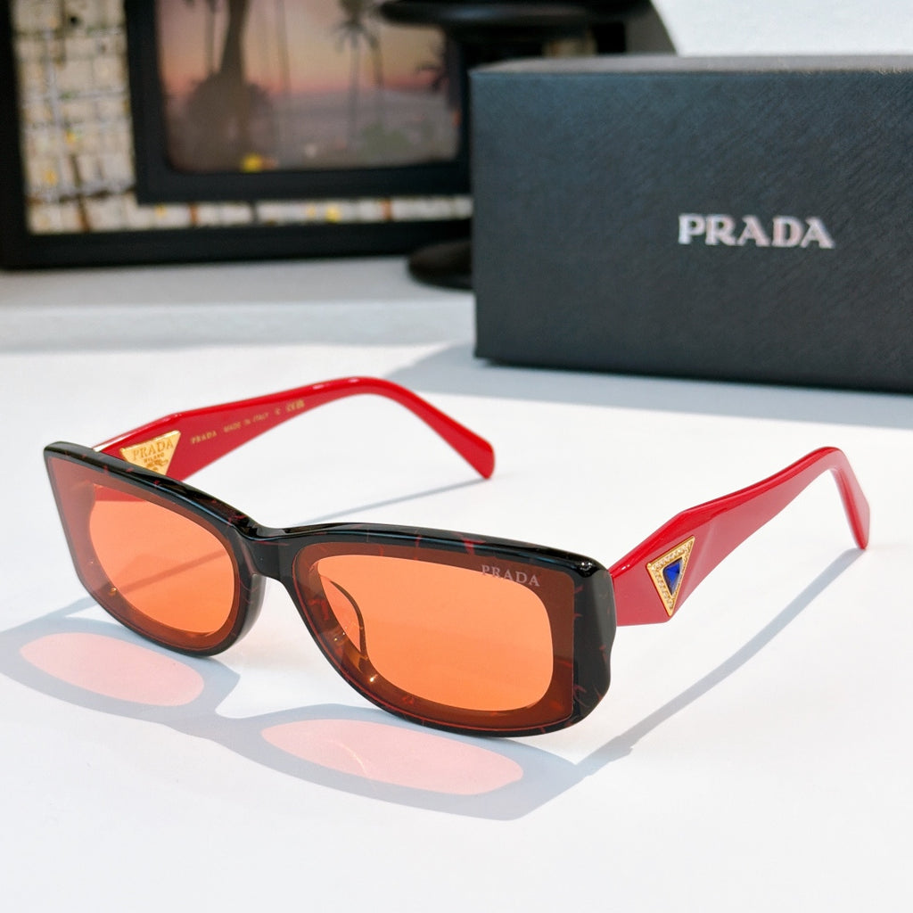 Sunglasses with red frame and orange-tinted lenses, gold triangle logo on temples.