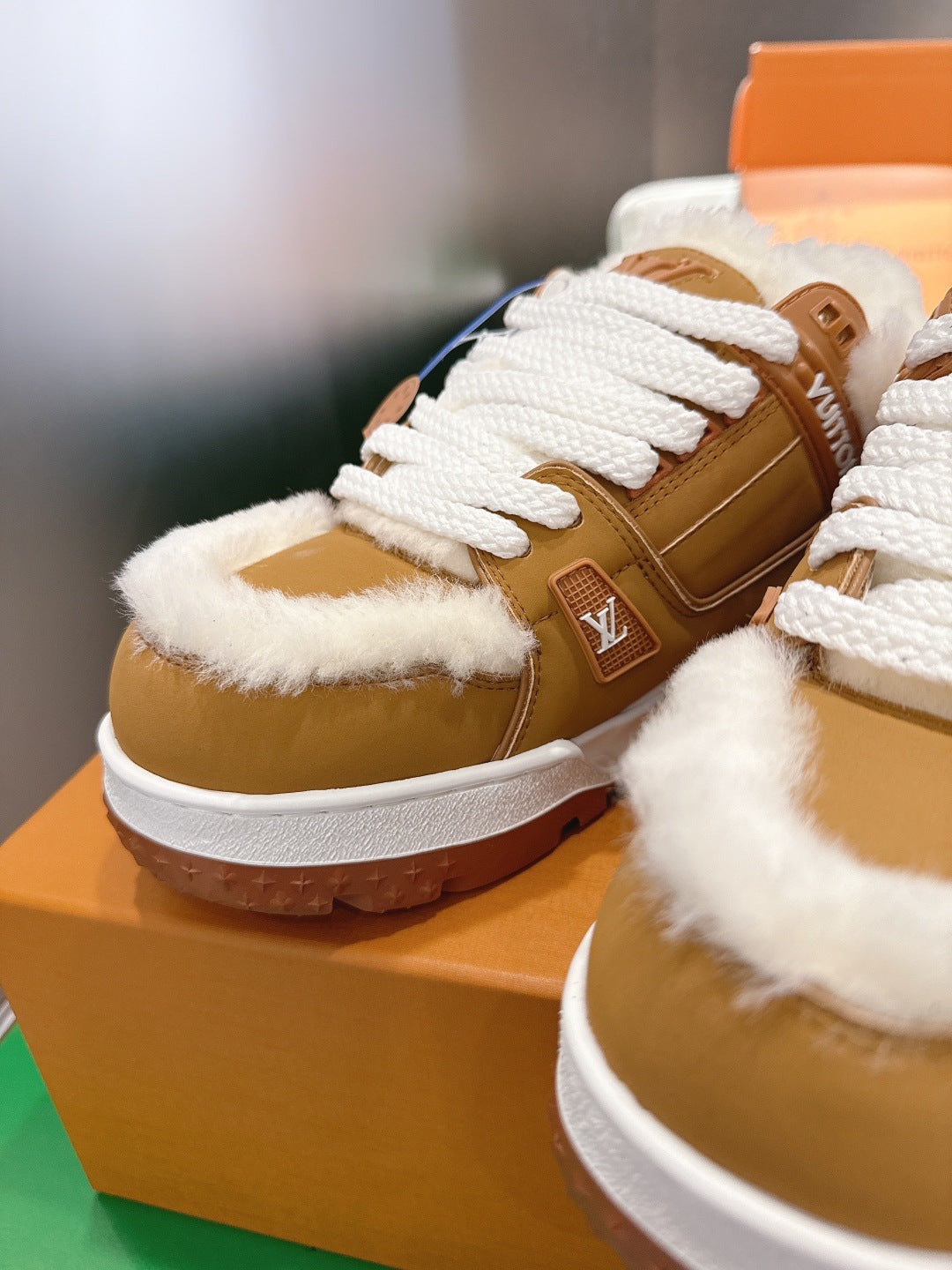 Unisex tan sneakers with white laces and fur trim, shown on a shoebox