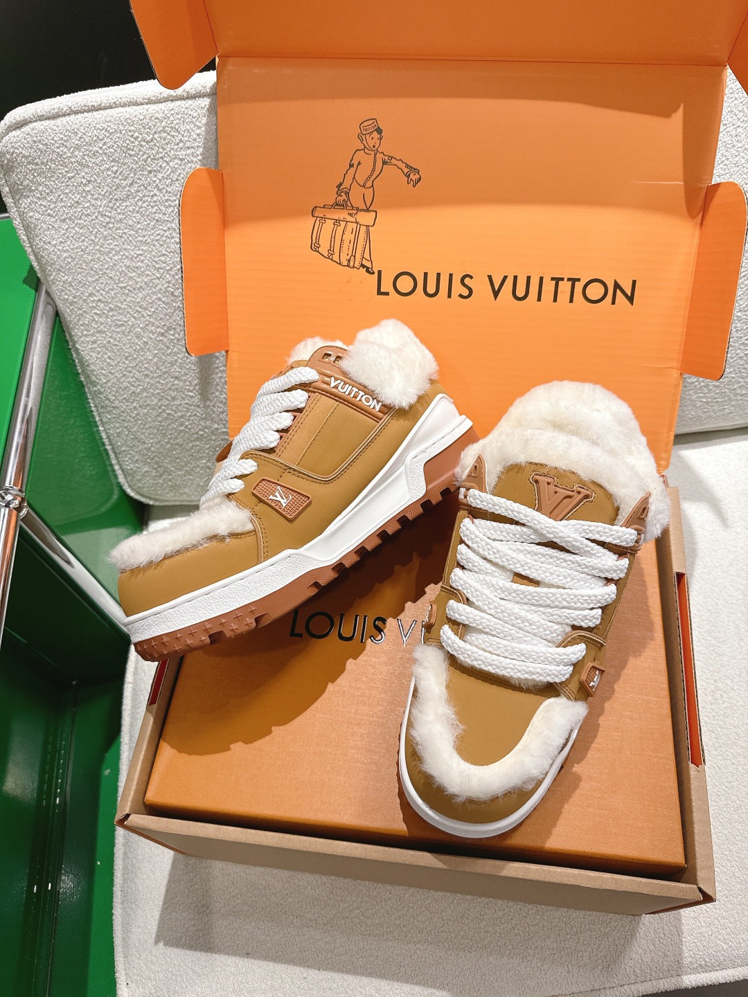 Unisex tan sneakers with white laces, fur trim, and chunky tread sole in box