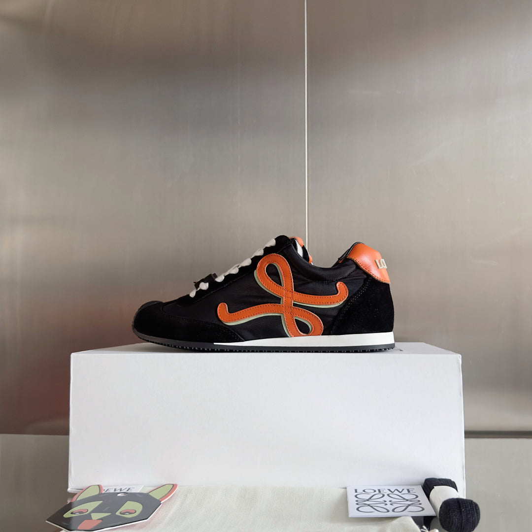 Unisex black low-top sneakers with orange emblem and white laces