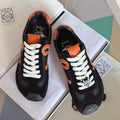 Unisex black sneakers with orange emblem and white laces, front and heel view