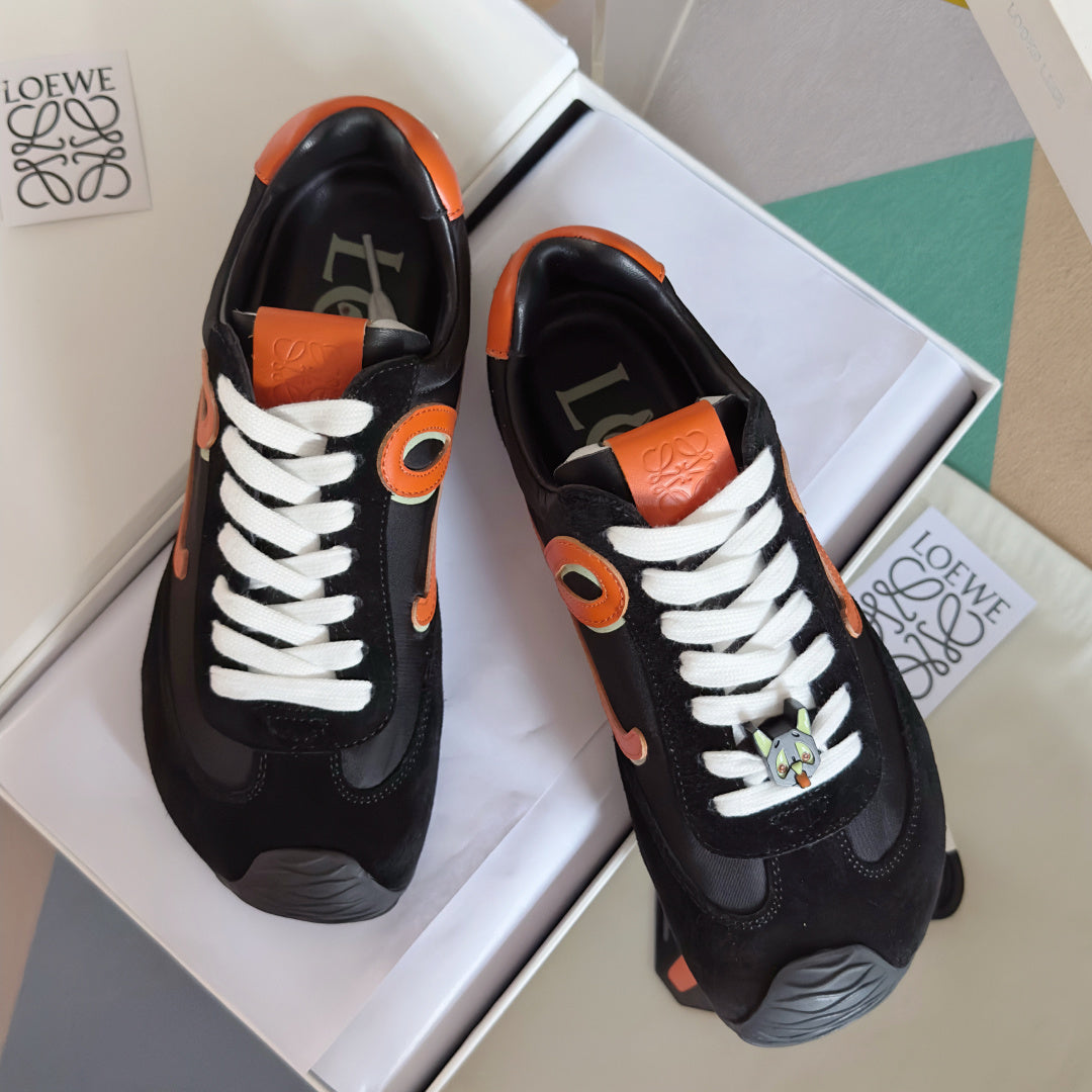 Unisex black sneakers with orange emblem and white laces, front and heel view