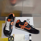 Unisex black low-top sneakers with orange emblem, white laces, and toe guard detail