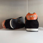 Unisex black sneakers with orange heel patch, white sole, and logo on back