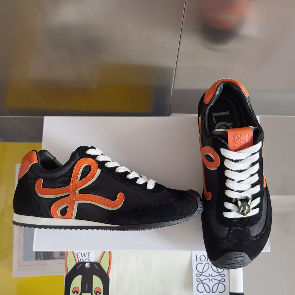 Unisex black sneakers with orange emblem, white laces, and patterned side detail