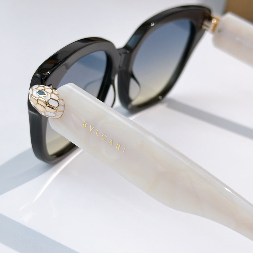 Black cat-eye sunglasses with clear temple, gold-tone emblem, and dark tinted lenses