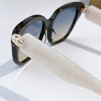 Black cat-eye sunglasses with clear temple, gold-tone emblem, and dark tinted lenses