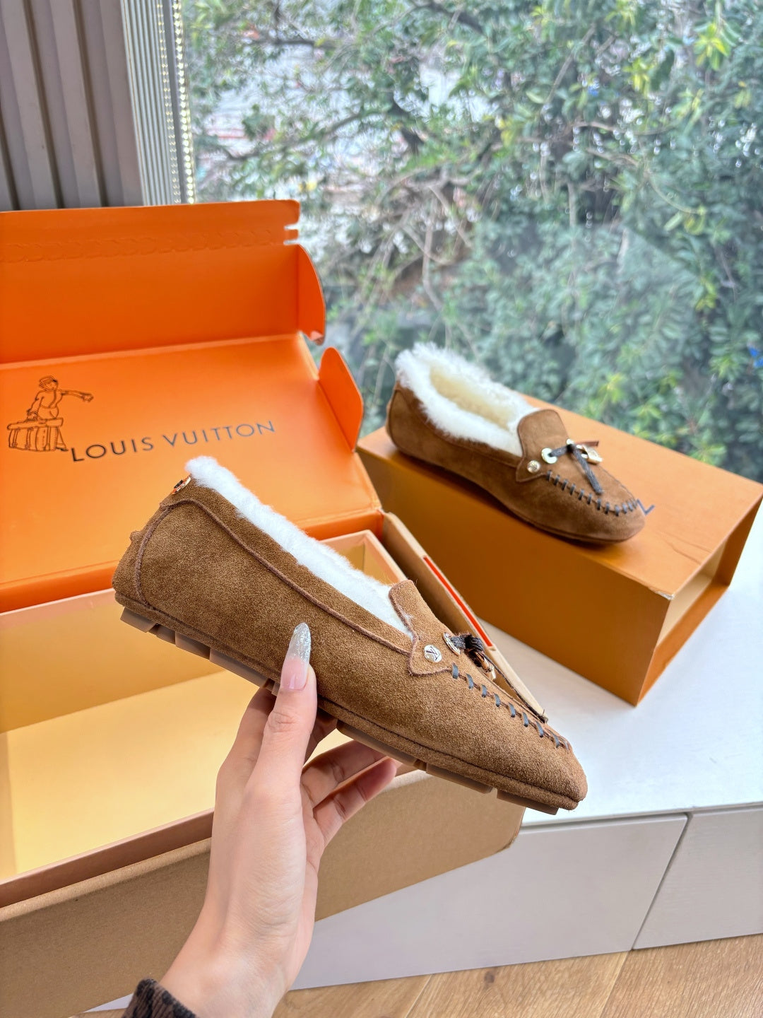 Brown suede shearling loafer, front view with stitched trim and metal charm detail