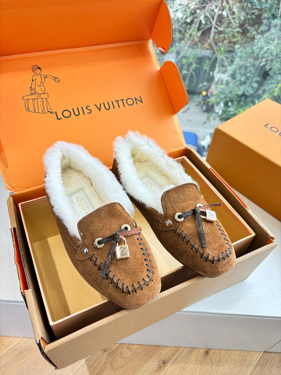 Brown suede shearling loafers with lace tie and stitched trim, two shoes in box