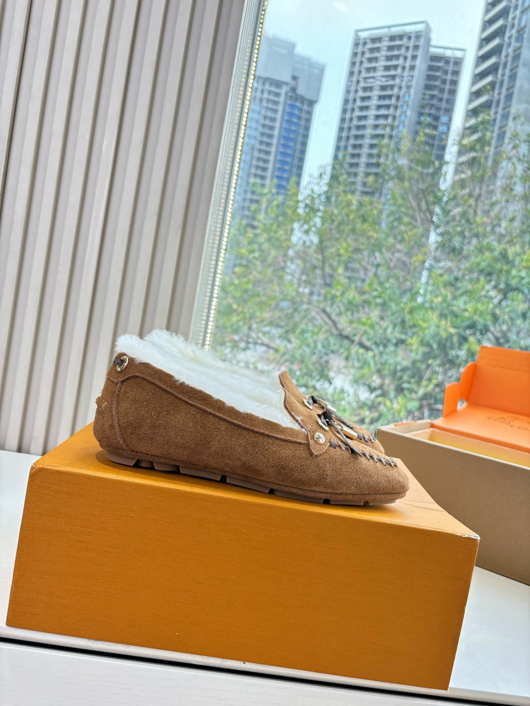 Brown suede shearling loafer on orange box, side profile with lace tie and charm