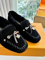 Close-up of black suede loafers with silver rope laces and LV charm