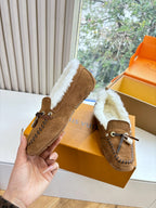 Brown suede shearling loafer in hand, with lace tie, stitched trim, and metal charm